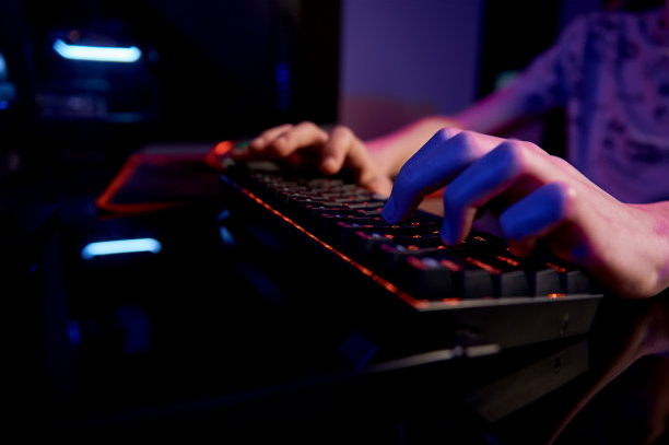 Profesionalni igralec igra računalniško videoigro v temni sobi, uporablja rgb mehansko tipkovnico neonske barve, prostor za kiberšportne igre